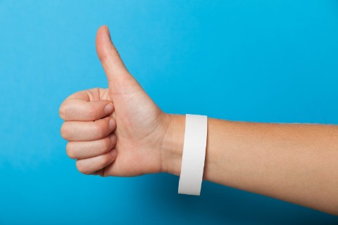 Hand on blue background making thumbs up gesture and wearing a white wristband.