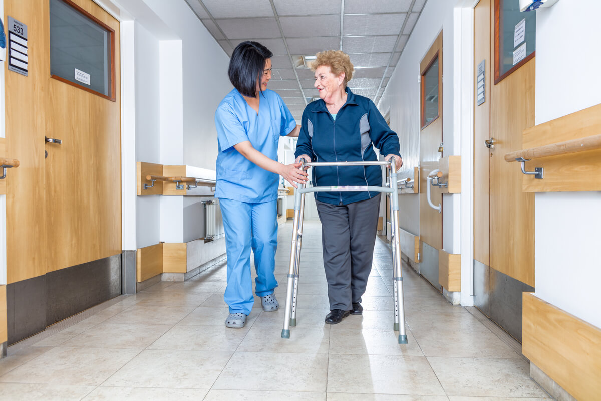 Nurse helps a patient walk down a hall.