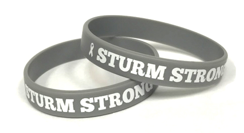 A gray printed wristband with a personal message saying sturm strong.